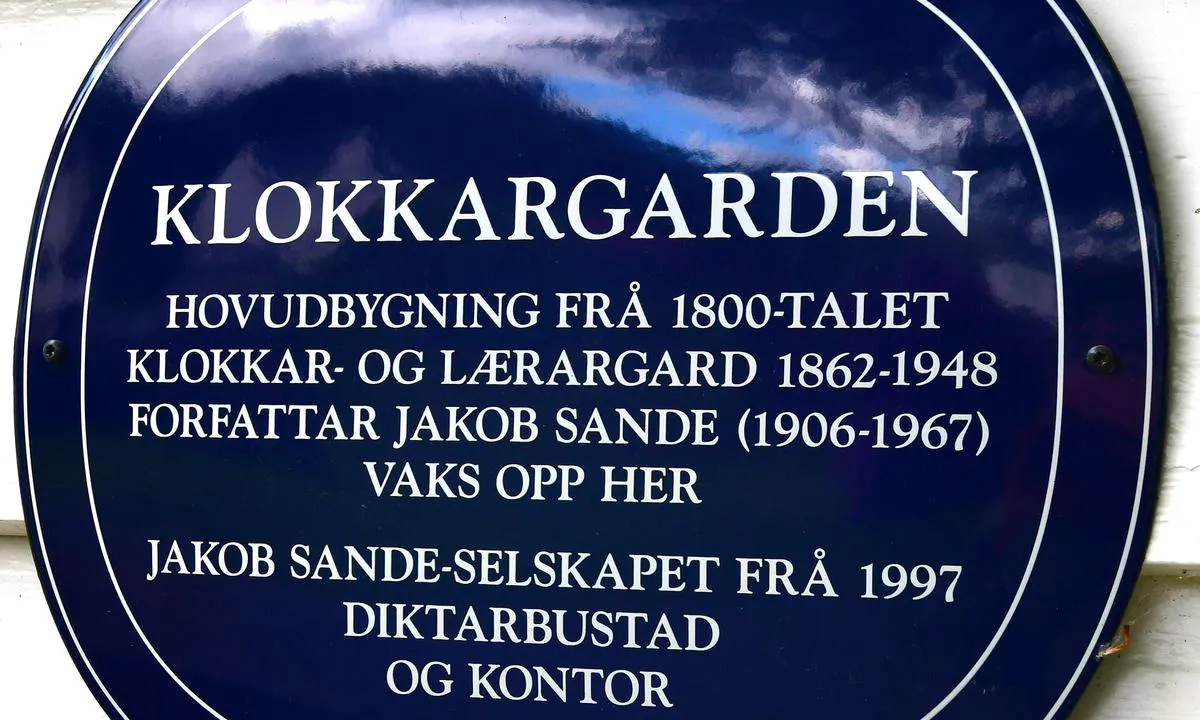 Bjergelandet Båthavn - Dale: {"base": "no", "no": "Skilt utanp\u00e5 Klokkargarden", "se": "Skylt utanf\u00f6r Klokkargarden", "en": "Sign outside Klokkargarden", "da": "Skilt udenp\u00e5 Klokkarg\u00e5rden"}