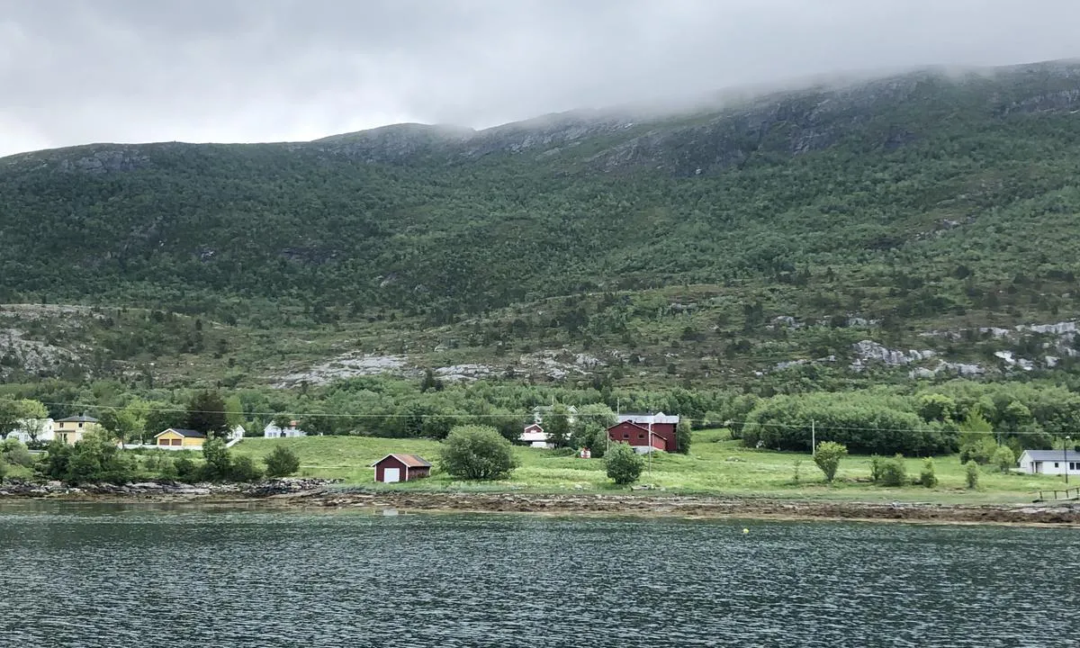 Gutvikvågen er lun og omkranset av fjell, spredt bebyggelse, kulturlandskap og en fergekai.