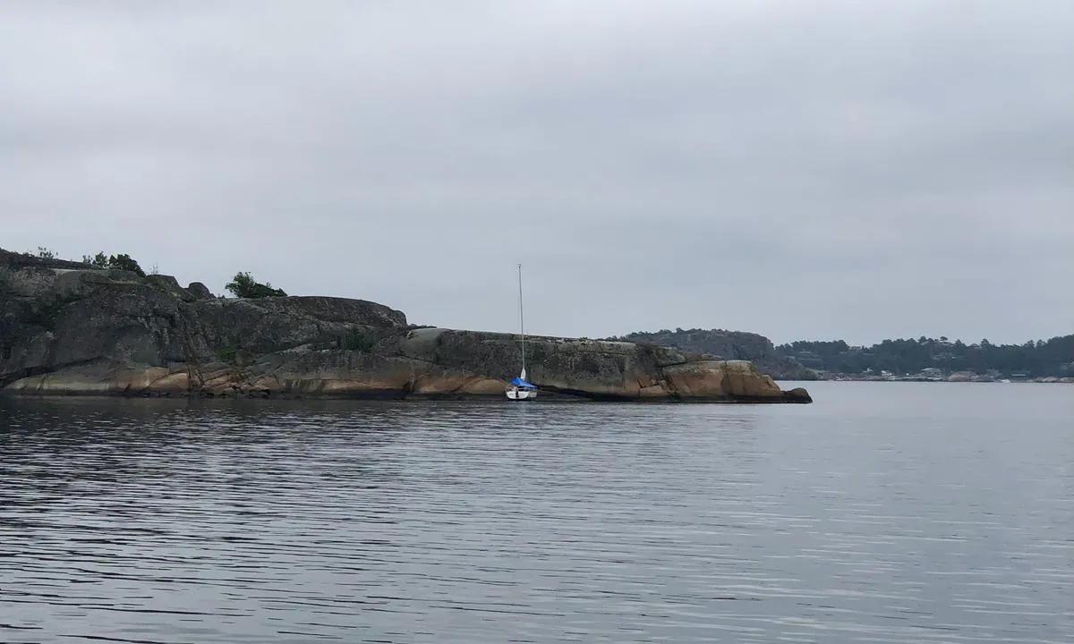 Liten seilbåt fortøyd med dregg inn mot land helt øst i Sperrvik.