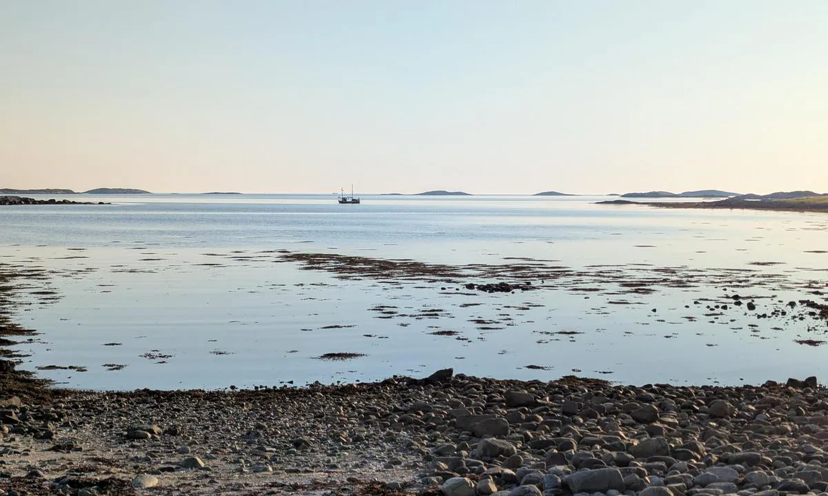 Strandskjæret: Båten på bildet ligger der ankringsplassen er markert i kartet. Det er OK dybde også litt lenger inn mot stranda med det hvite huset, men der ser det ut til å være mer småstein og vegetasjon på bunnen.