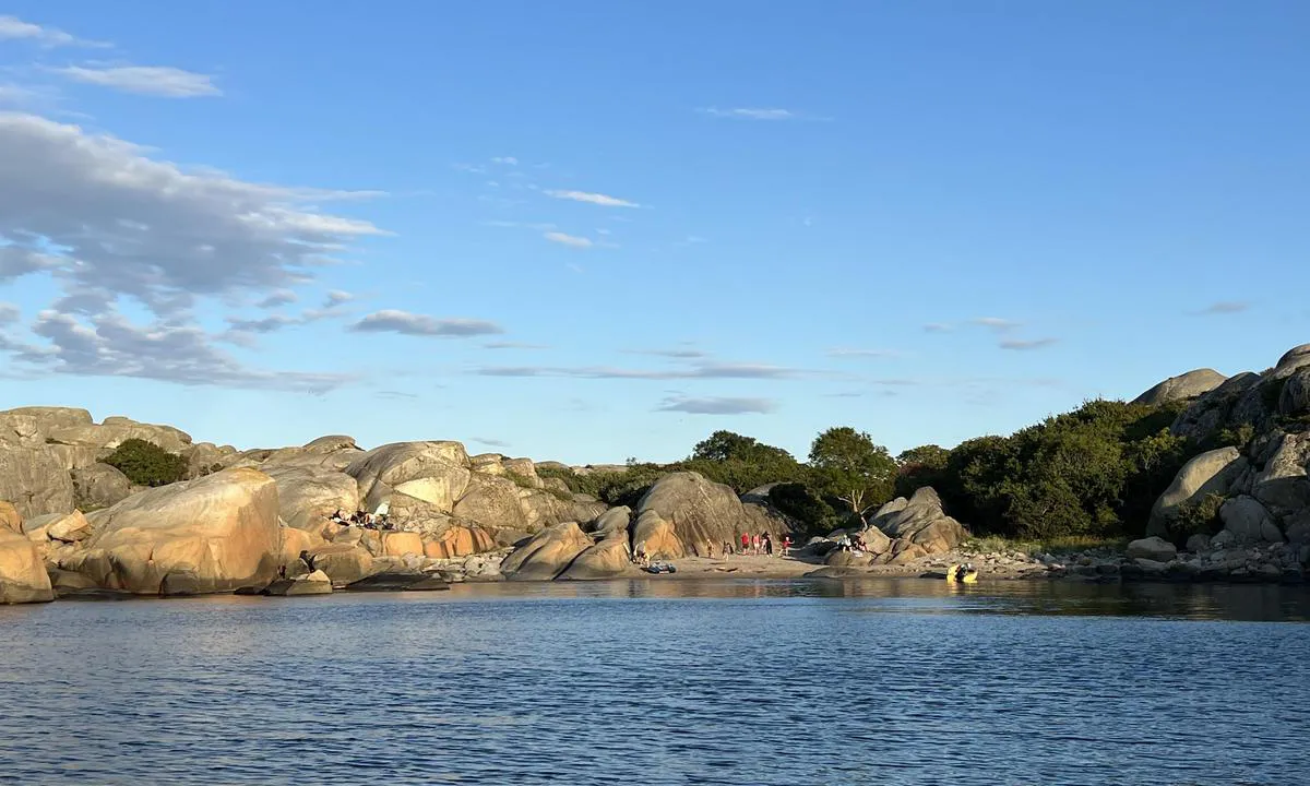 Svennerfyr stranda: Stranden innerst. Sti/gangvei opp under trærene midt i bildet, denne leder til fyrhavnen og fyret. Fortøyningsbolter i fjellet på østsiden (venstre i bildet) av bukten.